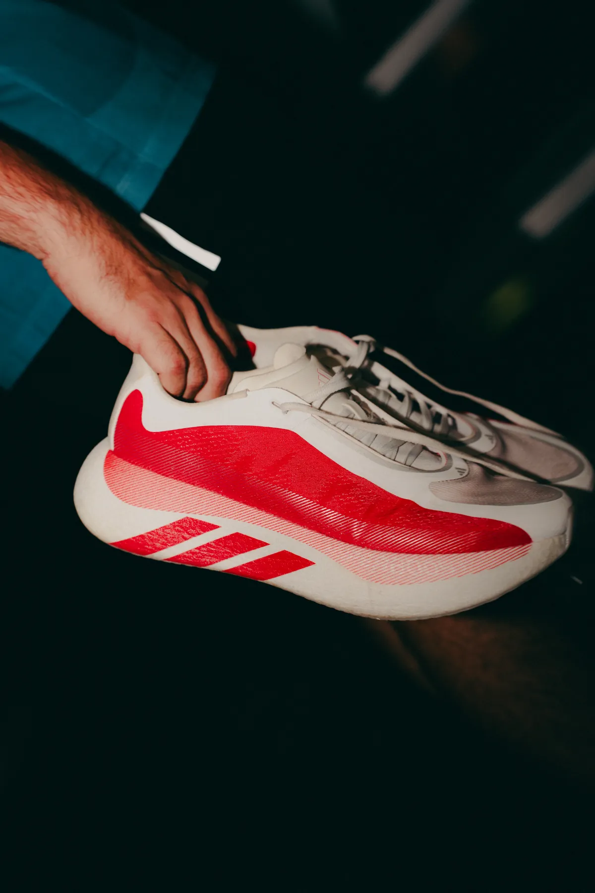 Mão segurando um tênis Adidas vermelho em fundo escuro